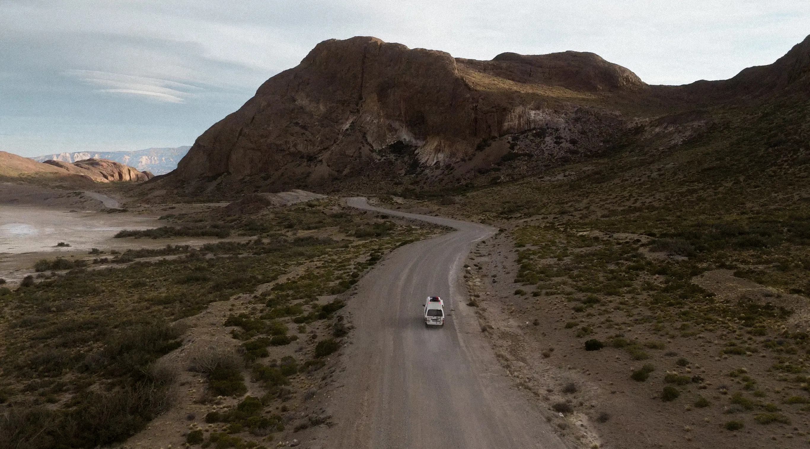 Prise de vue aérienne du van sur une piste de terre au pied d'une barre rocheuse