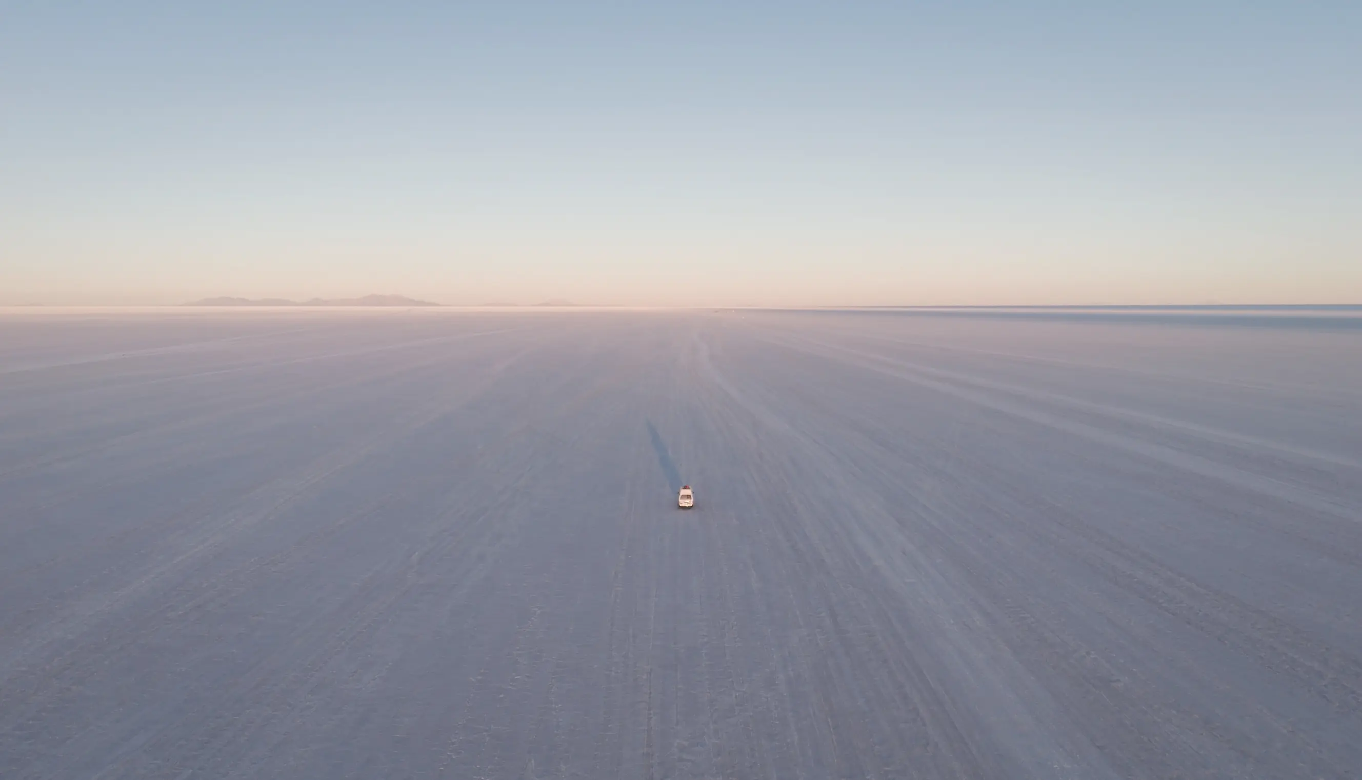 Prise de vue aérienne du van qui traverse le Salar d'Uyuni au lever de soleil